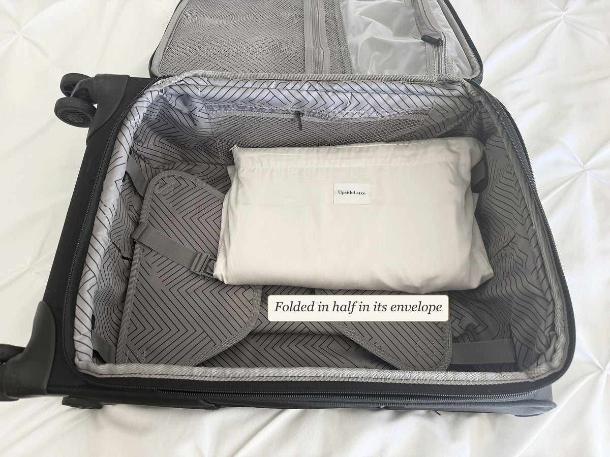 UpsideLuxe Sleep Sack in its envelope, folded in half inside a carry-on suitcase